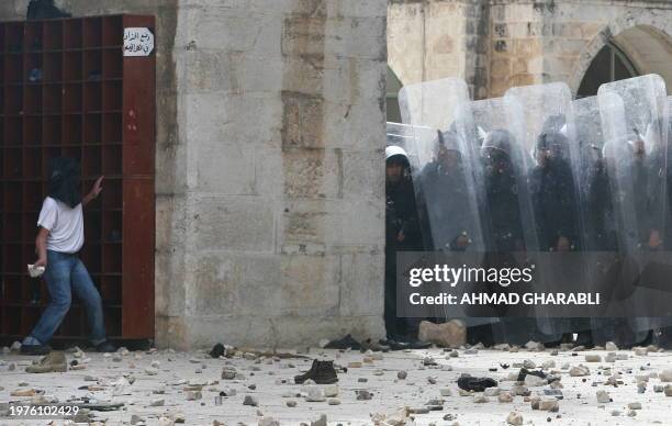 Masked Palestinian youth throws a stone towards Israeli police standing near the entrance of the Al-Aqsa mosque during clashes on March 5, 2010 at...