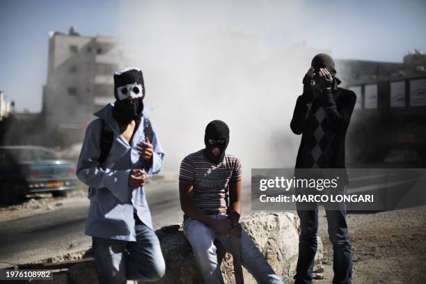 Masked Palestinian youths are seen enveloped by dust from a passing lorry on November 9, 2010 during clashes with Israeli forces in the Arab village...