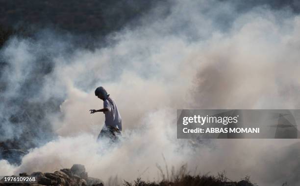Masked Palestinian stone thrower stands amidst tear gas smoke during clashes against Israeli soldiers following a weekly demonstration against...