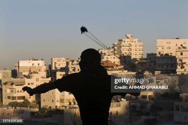 Masked Palestinian youth hurls a stone at Israeli border police during clashes in the east Jerusalem Arab neighbourhood of Issawiya on December 3,...