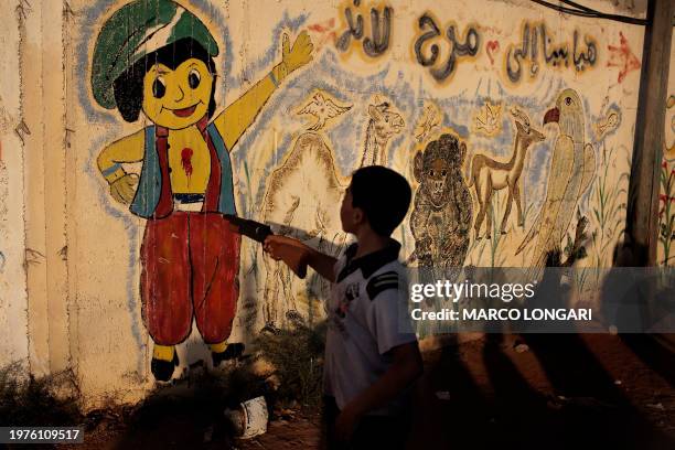 Palestinian child points his toy gun at a mural daubed with red paint giving the impression of the character being shot in the heart, at an amusement...