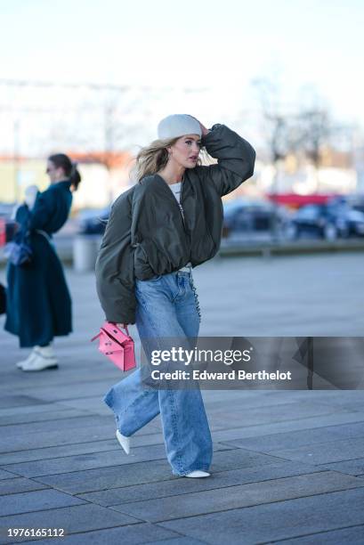 Emili Sindlev wears a white hat, a green bomber jacket, a pink Hermes bag, flared denim jeans pants, white pointed shoes, outside OperaSport, during...