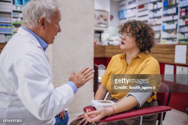 pharmacist measuring blood pressure to woman - hypertensive stockfoto's en -beelden