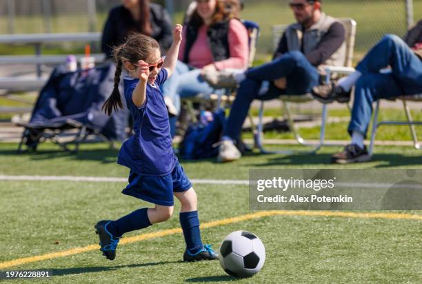 aufgeregtes, kleines mädchen, das auf dem feld fußball spielt. - jugendfußball stock-fotos und bilder