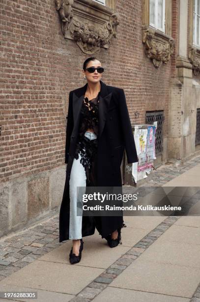 Darja Barannik wears blue jeans, a sheer black top and black long coat outside The Garment during the Copenhagen Fashion Week AW24 on January 31,...