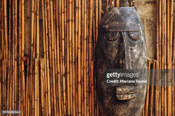 native mask hangs in a wall of small bamboo sticks. - gimp mask stock pictures, royalty-free photos & images