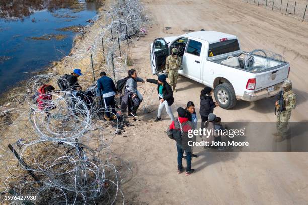 Seen from an aerial view, Texas National Guard troops watch as immigrants pass through razor wire after crossing the U.S.-Mexico border into El Paso,...