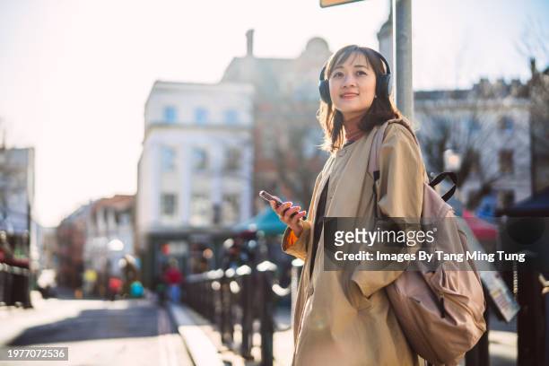 asian businesswoman with headphone using mobile app to book a taxi ride on smart phone while waiting in city street - recreational equipment stock pictures, royalty-free photos & images
