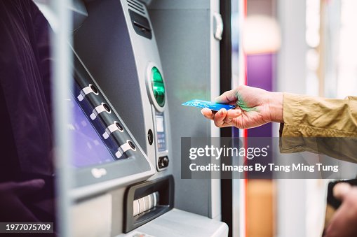 Female hand inserting bank card into automatic cash machine (ATM) to access bank account services in the city Female hand inserting bank card into automatic cash machine (ATM) to access bank account services in the city