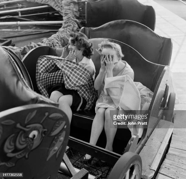 British stage school student Patricia Stark and British actress Barbara Windsor both cover their faces as they ride the Caterpillar at the funfair in...