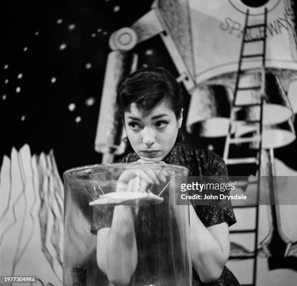 British actress Natasha Parry rests her head on the helmet of a Martian spacesuit as she waits for her cue during the filming of 'You Know What...