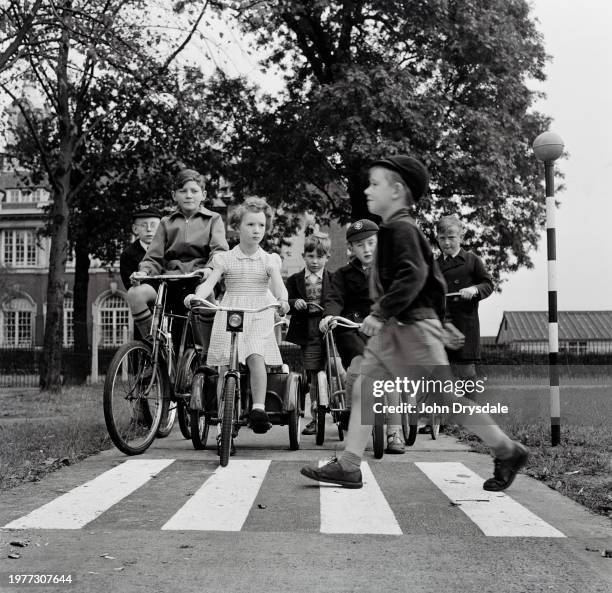 Child cyclists wait at a miniature pedestrian crossing as a young boy crosses during a road safety class in Wood Green, London, England, 1955.