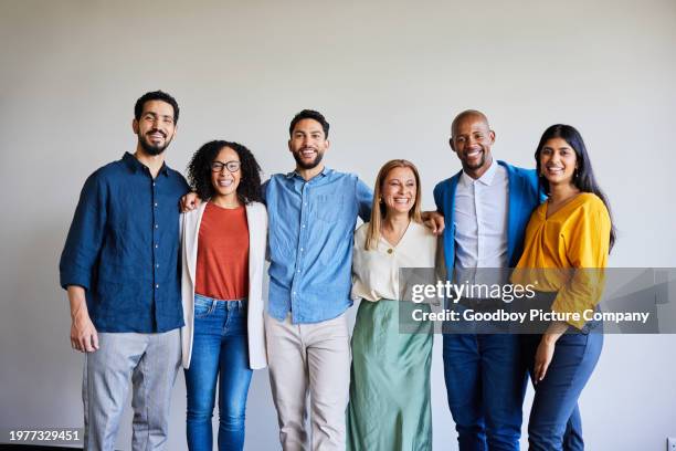 diverse businesspeople smiling while standing arm in arm in an office - employee photo wall stock pictures, royalty-free photos & images