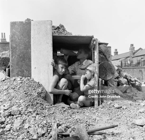 Children drinking juice from bottles inside a den at the Lollard Adventure Playground in Lambeth, London, August 1955. The children at front are...