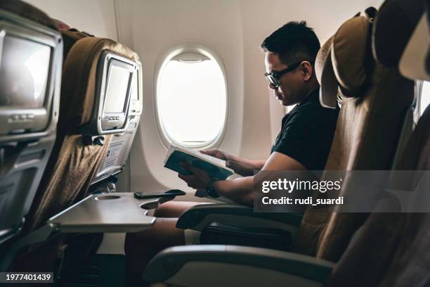 man reading a book on airplane - asian man holding book stock pictures, royalty-free photos & images