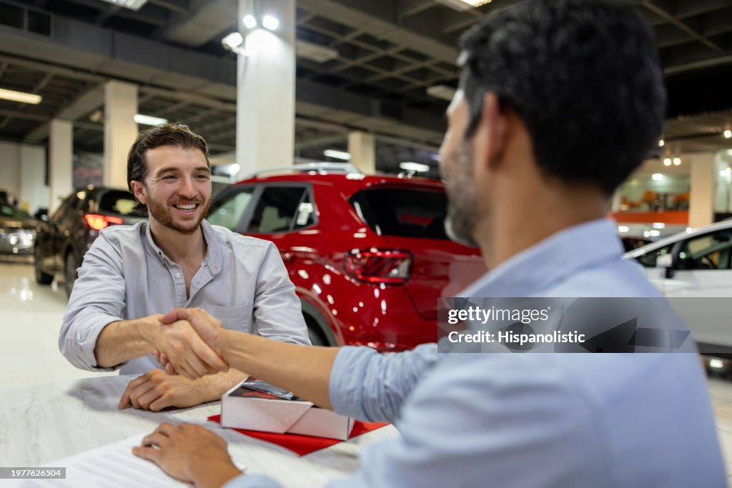 Man buying a car and closing the deal handshaking the salesman