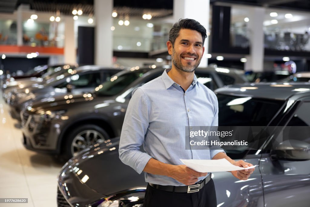 Happy salesman working at a car dealership holding a lease agreement