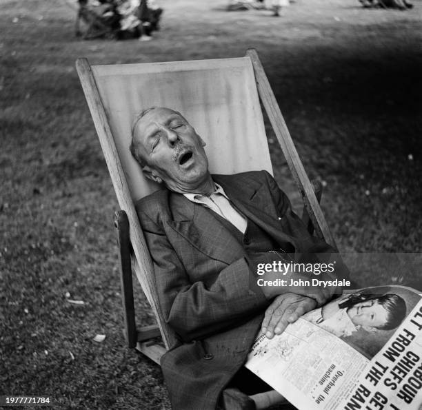 Man asleep with his mouth open, a newspaper across his lap, as he sits in a deckchair on a Thames towpath at Richmond, London, England, August 1955.