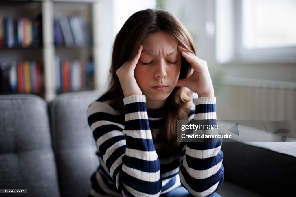Unhappy young woman sitting on sofa, thinking of problems