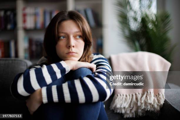 sad unhappy teenage girl embracing knees, sitting alone on couch - conspiracy stock pictures, royalty-free photos & images