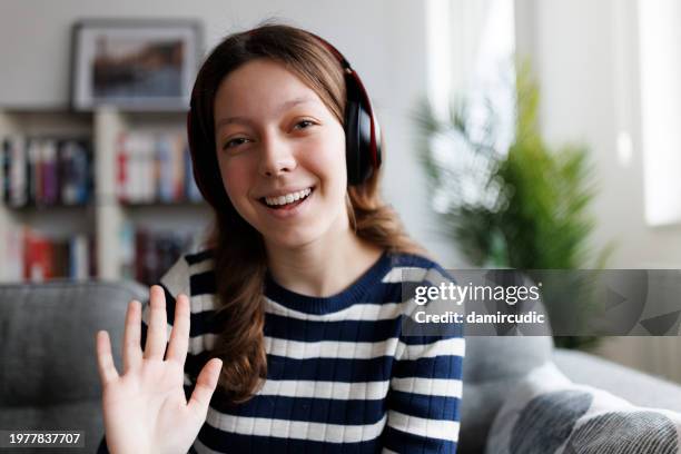 adolescente sonriente con auriculares bluetooth saludando con la mano en videollamada en casa - video chat with girl fotografías e im�ágenes de stock