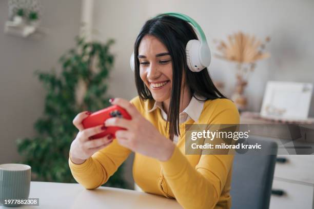 young woman playing video games on her phone with headphones on - mobile game stock pictures, royalty-free photos & images