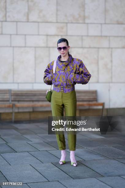 Candice Burgi wears sunglasses, a purple and khaki ribbed gathered puff oversized jacket , a green bag, khaki pants , pink socks, pointed shoes,...