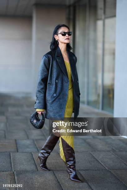 Pornwika Spiecker wears sunglasses, a black oversized leather jacket, a yellow ribbed dress , a black leather Miu Miu bag, high heels brown crocodile...