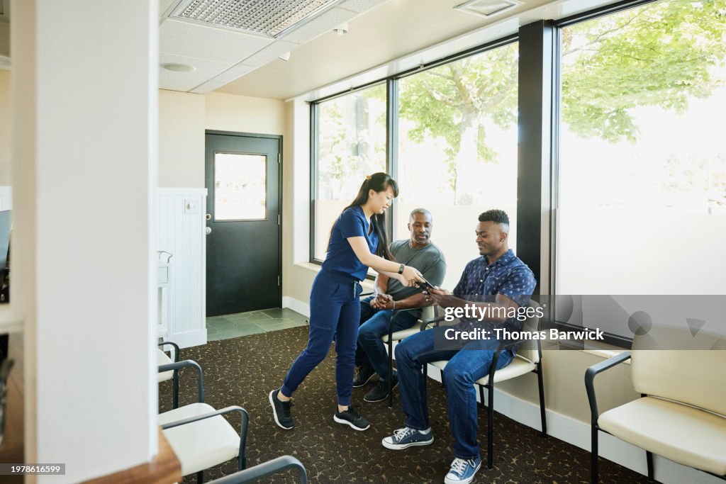 Wide shot nurse handing digital tablet to patient in waiting room