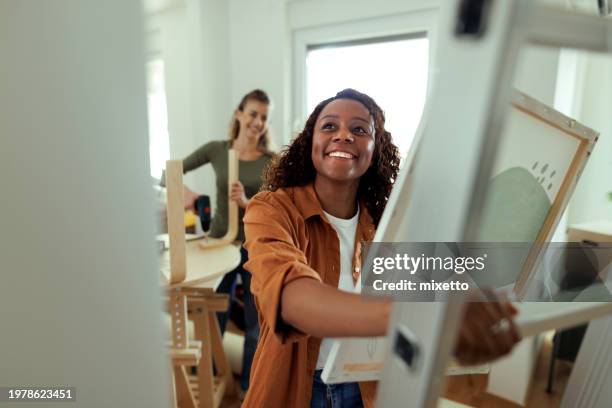 giovane donna sorridente che decide dove mettere l'immagine nel nuovo appartamento - trasferimento dimmagine foto e immagini stock