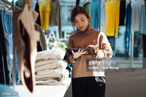 young asian saleslady taking inventory with digital tablet in retail shop - fashion industry stock pictures, royalty-free photos & images