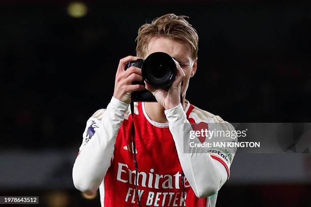 Arsenal's Norwegian midfielder Martin Odegaard picks up a camera and takes pictures as he celebrates at the end of the English Premier League...