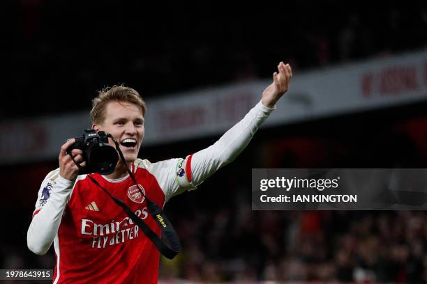 Arsenal's Norwegian midfielder Martin Odegaard picks up a camera and takes pictures as he celebrates at the end of the English Premier League...