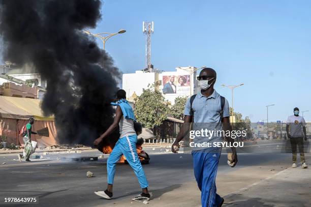 Opposition supporters holding stones walk next to a burning barricade during demonstrations called by the opposition parties in Dakar on February 4,...