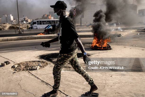 Man walks pat burning tyres during demonstrations called by the opposition parties in Dakar on February 4 to protest against postponement of the...