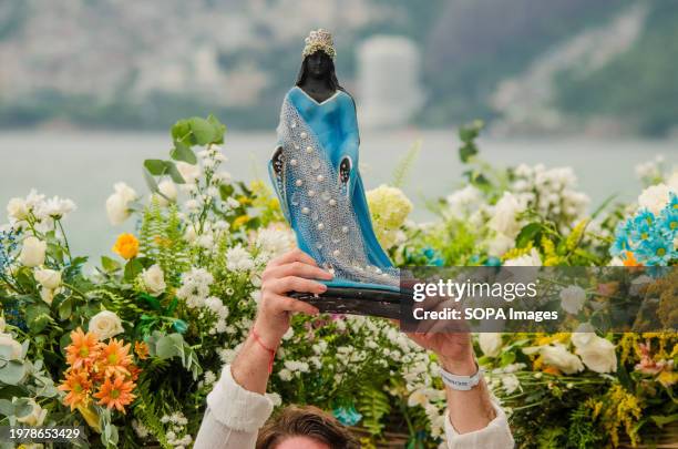 Devotee holds the statue of Iemanjá with flowers behind on Iemanjá's day. Every year, across the country, Brazilians of all faiths gather to...