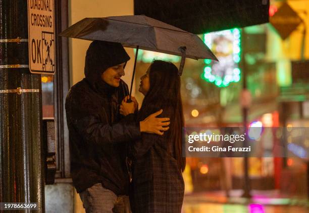 Couple share space and an umbrella at a cross walk as heavy rain fall off Colorado Boulevard on February 4, 2024 in Pasadena, California. The heavy...