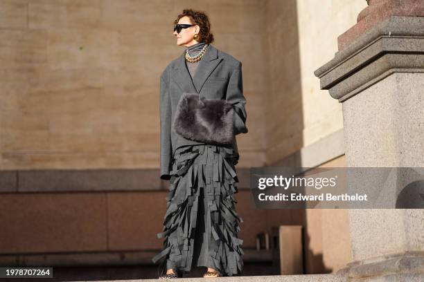 Renia Jaz wears sunglasses, golden earrings, a gray turtleneck top, a gray oversized blazer jacket , a fluffy bag, fringed skirt , outside Marimekko,...