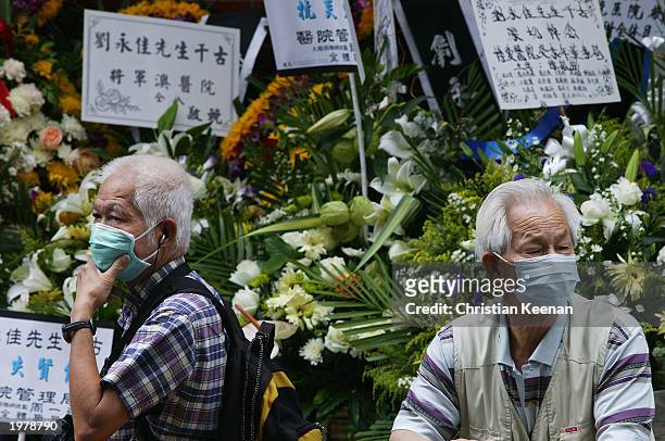 Onlookers stand in front of bank of wreathes during the funeral of Hong Kong's first nurse killed by SARS , Mr Lau Wing-Kai at Gallant Garden, a...