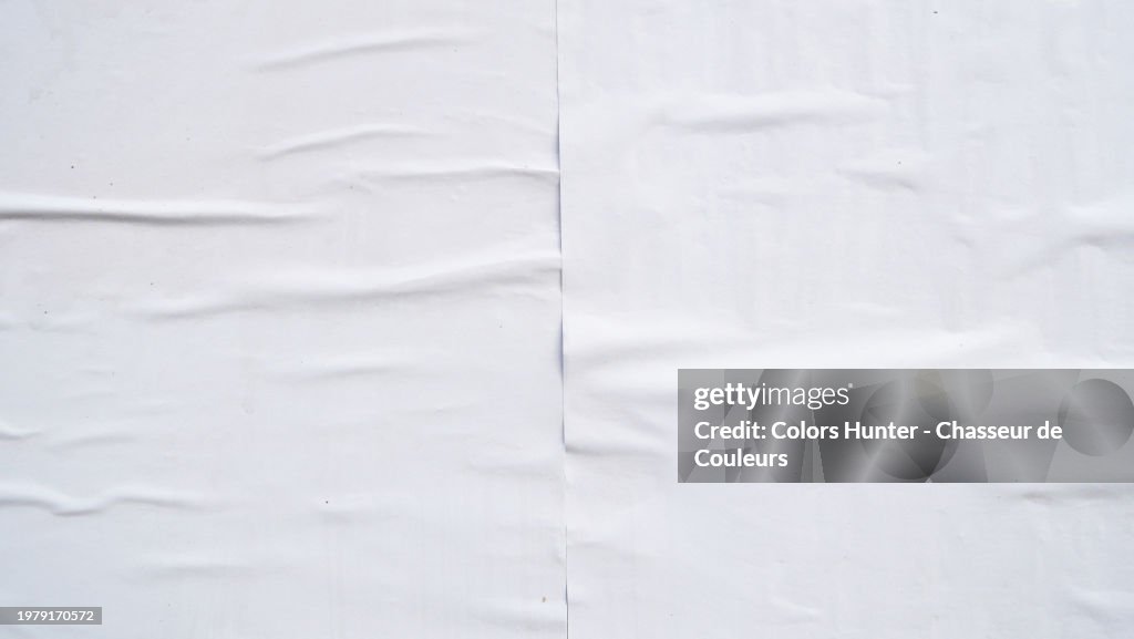 Close-up of two white posters glued side by side on a wall and rippled in Paris, France. Sunlight. Natural colors.