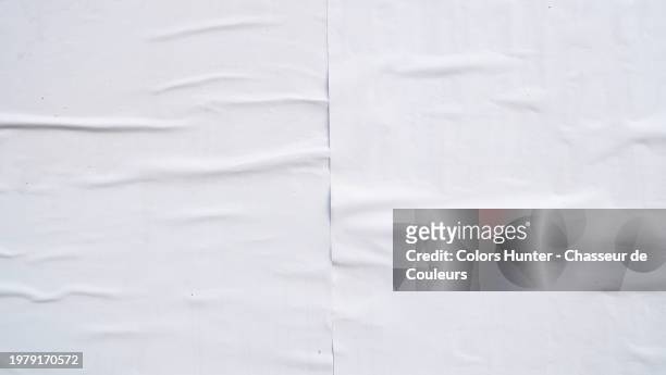 close-up of two white posters glued side by side on a wall and rippled in paris, france. sunlight. natural colors. - side by side billboard stock pictures, royalty-free photos & images