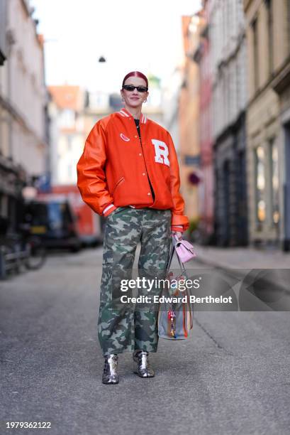 Marianne Theodorsen wears sunglasses, earrings, an orange Teddy jacket , a t-shirt, green khaki military camouflage printed pattern pants , silver...