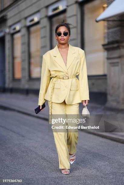 Ellie Delphine wears sunglasses , a pastel pale yellow oversized blazer jacket , a belt, flared pants , outside Mark Kenly Domino Tan, during the...