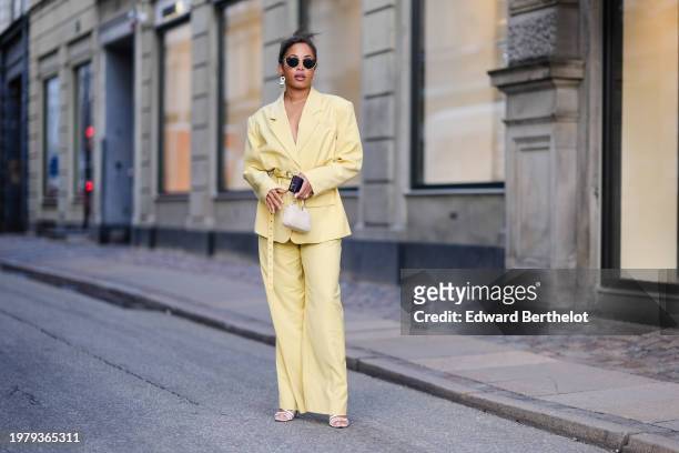 Ellie Delphine wears sunglasses , a pastel pale yellow oversized blazer jacket , a belt, flared pants , outside Mark Kenly Domino Tan, during the...