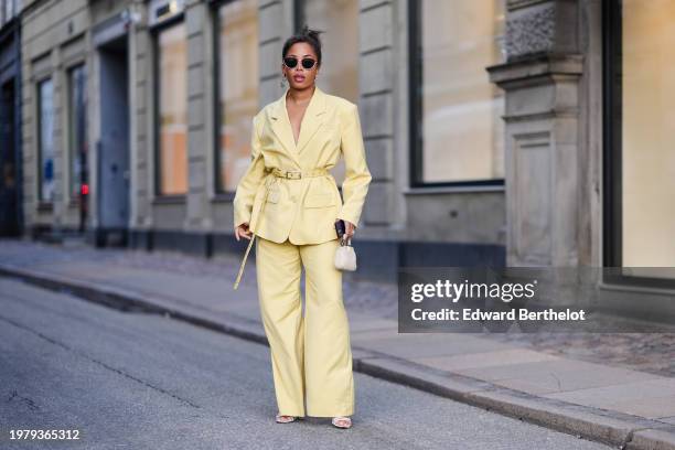 Ellie Delphine wears sunglasses , a pastel pale yellow oversized blazer jacket , a belt, flared pants , outside Mark Kenly Domino Tan, during the...