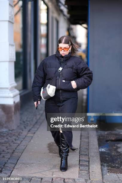 Guest wears sunglasses , a black bomber oversized puffer jacket , black slit denim skirt , knee high black leather boots , during the Copenhagen...