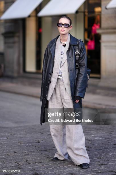 Guest wears sunglasses a black long leather jacket, a gray oversized blazer jacket , suit flared pants , outside Mark Kenly Domino Tan, during the...