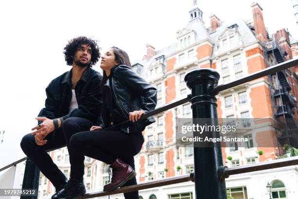 stylish couple sitting on urban railing - denim coat stock pictures, royalty-free photos & images