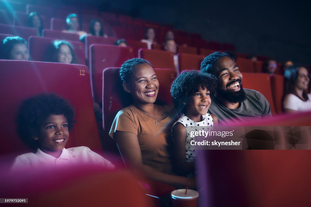 Happy black family watching a movie projection in theatre.