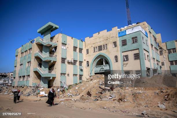 People walk past Al-Rantissi hospital on February 3 that was damaged during Israeli bombardment on Gaza City, as battles continue between Israel and...